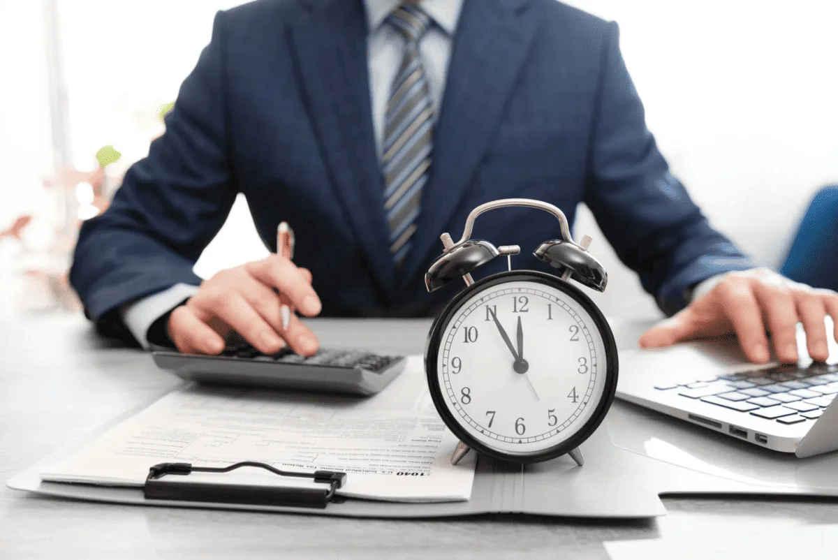 Businessperson calculating payroll with a clock on a desk, representing exempt employee classification and time tracking