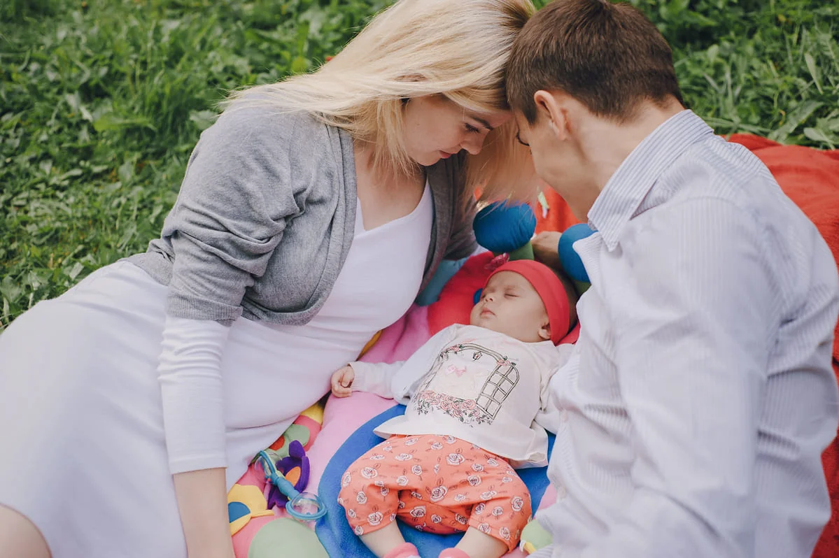 Parents bonding with newborn during FMLA family leave Parents lying on a blanket in the grass with their newborn baby, representing family bonding and parental leave.