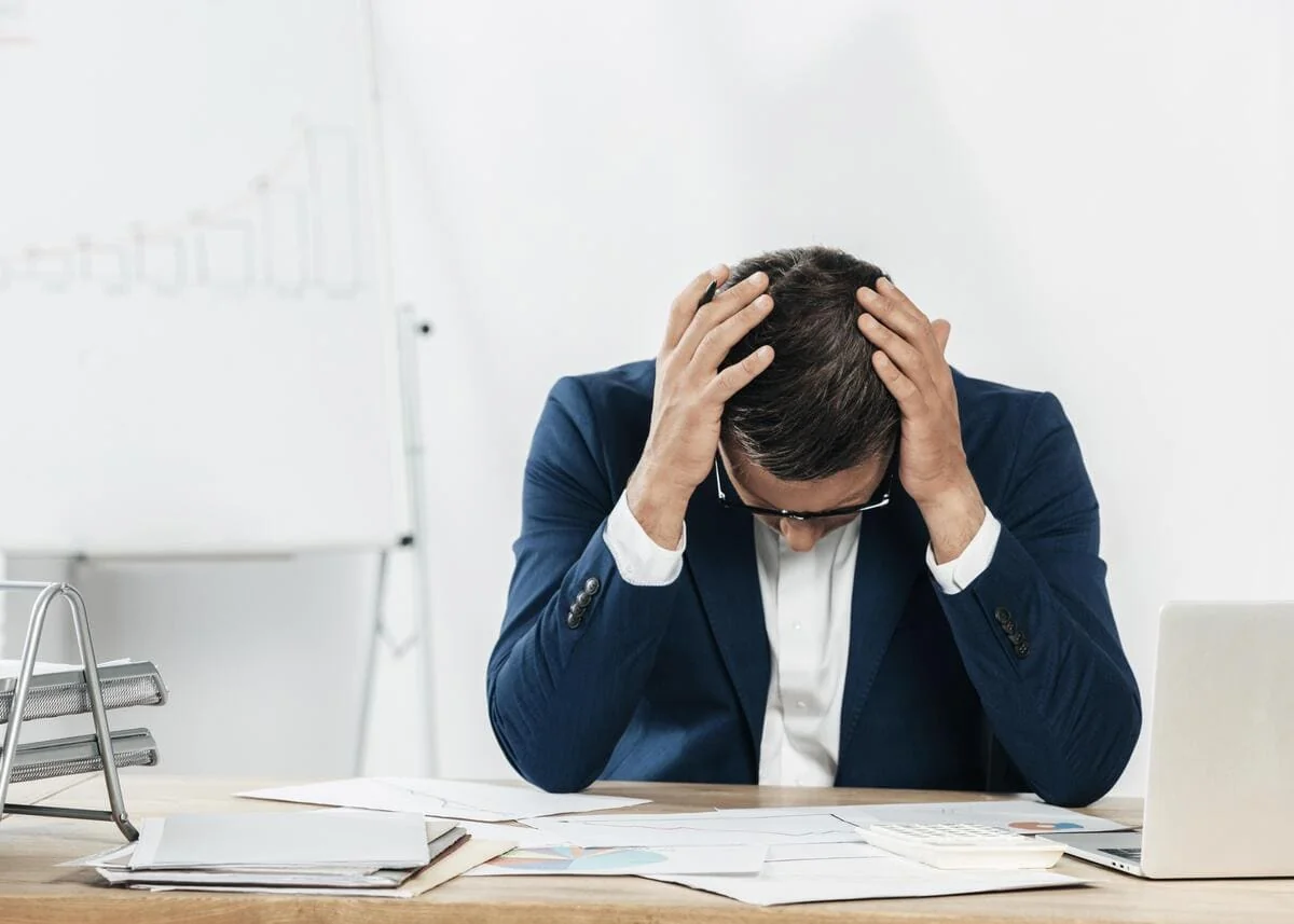 Frustrated business owner holding head in hands over misclassification paperwork