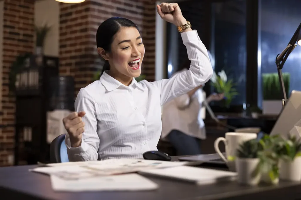 Employee celebrating at a desk after finishing work, showing the impact of accurate time tracking and payroll