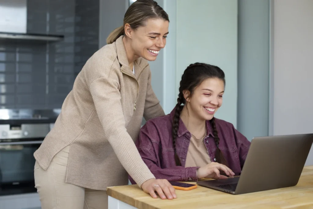 two female employees using a Free Time Tracking Software are smiling at laptop screen