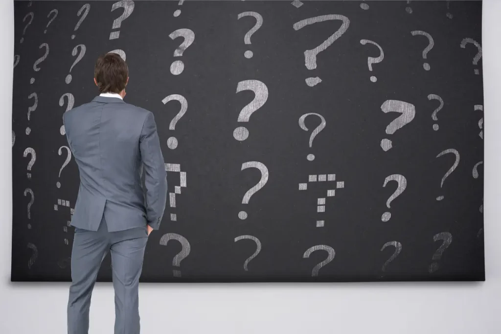 Business professional standing in front of a wall of question marks while evaluating a decision about which time tracking software to use