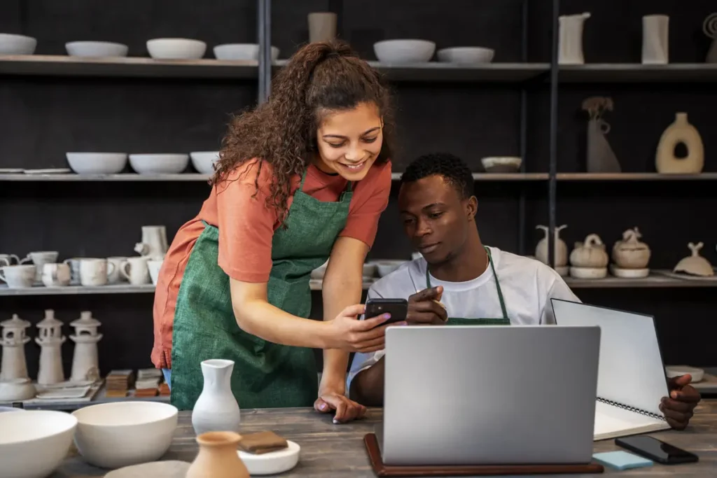 Two small business employees reviewing information on a laptop and smartphone together