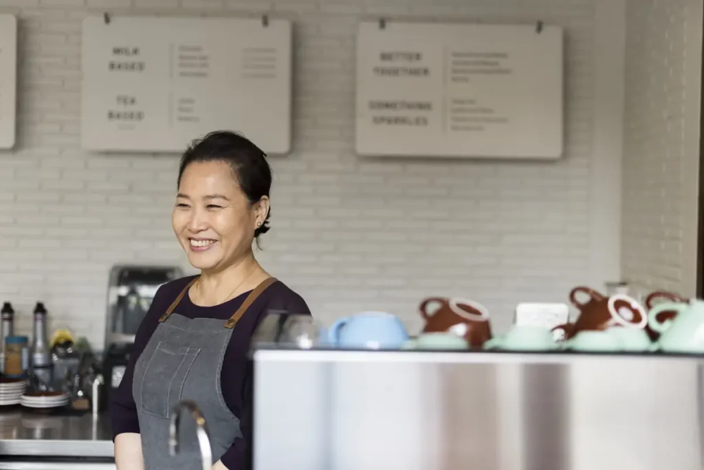 Small business owner smiling behind counter after simplifying payroll with time tracking software