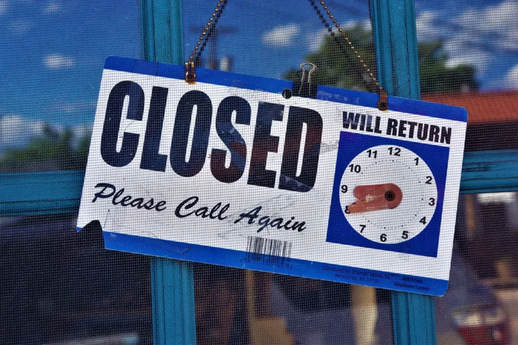 Closed sign with a will return clock hanging on a shop door